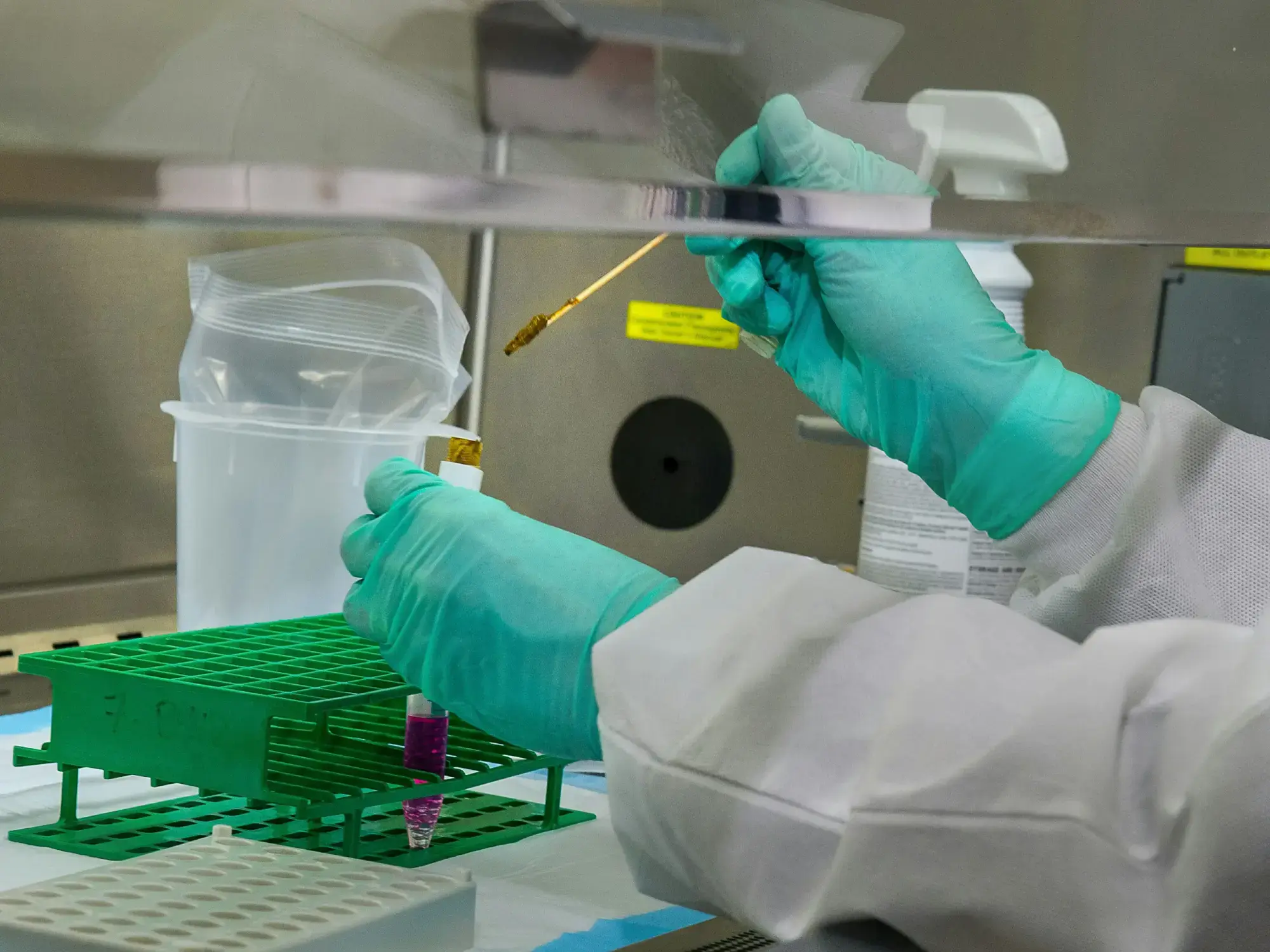 Gloved hand holding test tube near industrial water treatment facility